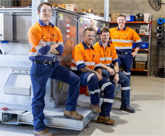 Careers - Four Electrical Engineers smiling beside Electrical Control Panel and Instrumentation Equipment at Milek Engineering